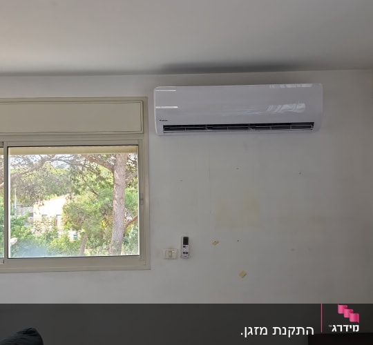 מזגן עילי לבן מותקן על קיר בחדר מגורים מעל חלון